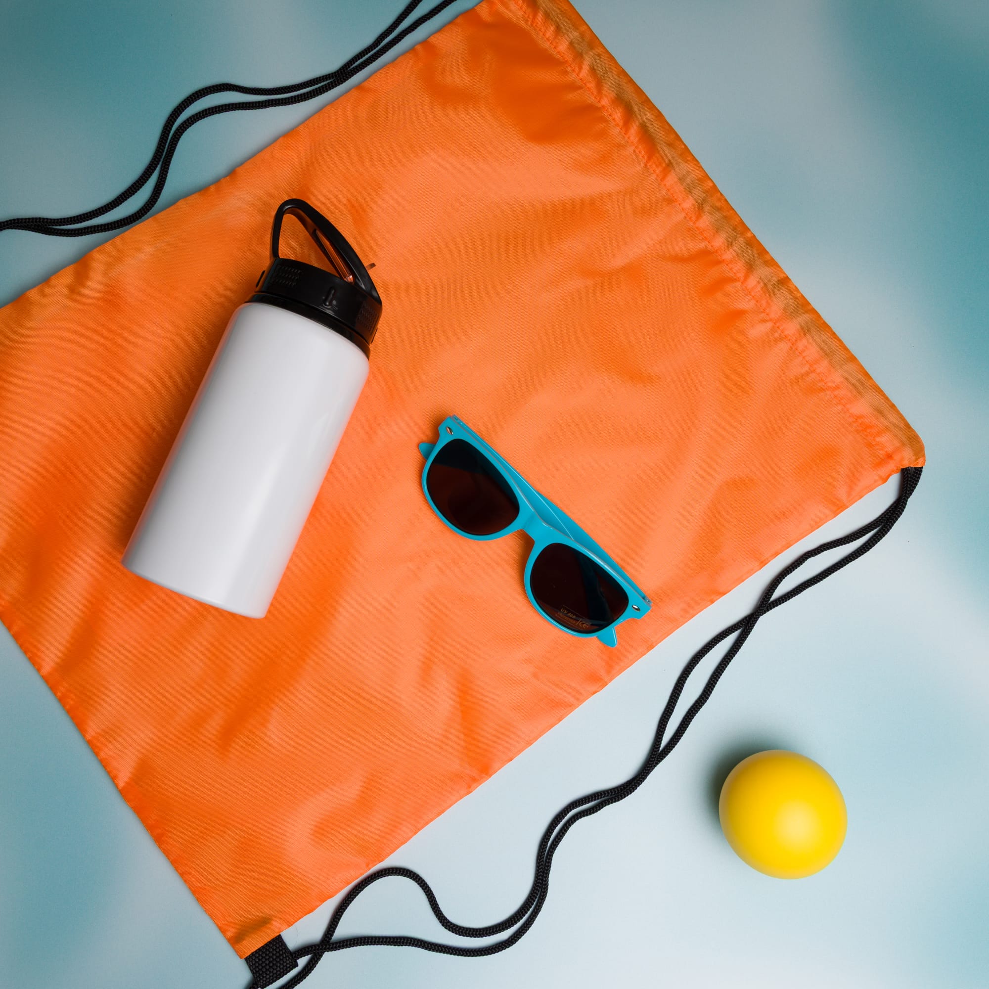 A drink bottle, a pair of turquoise sunglasses, and a yellow ball are laid out on an orange drawstring bag.