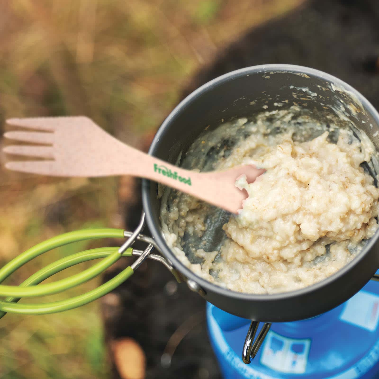 A cooking pot containing a creamy mixture with a green handle and a wooden fork labeled 