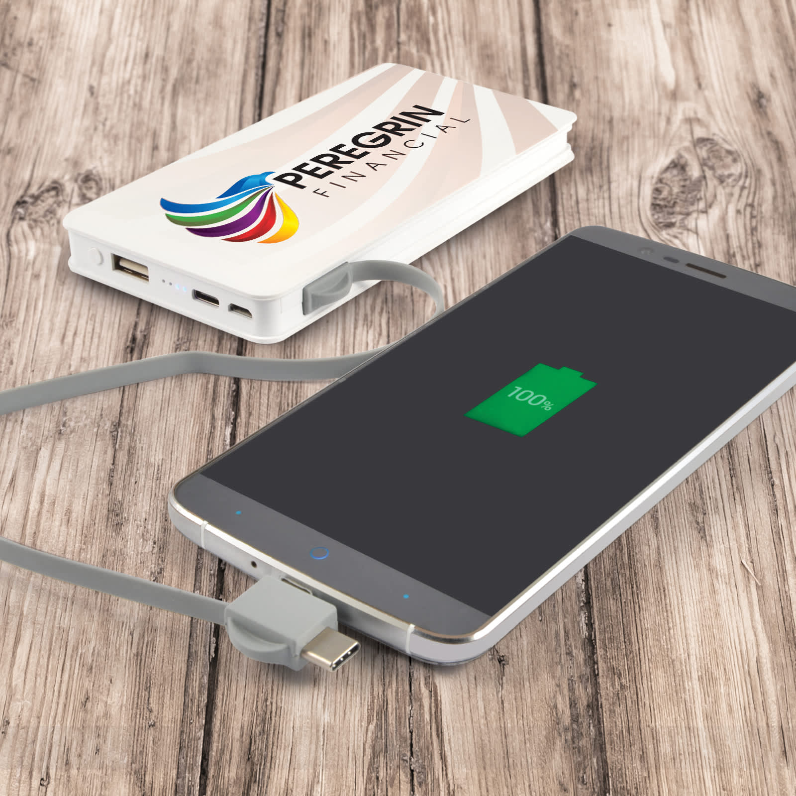 A white power bank with multiple ports, connected to a smartphone displaying a full battery icon on a wooden surface.