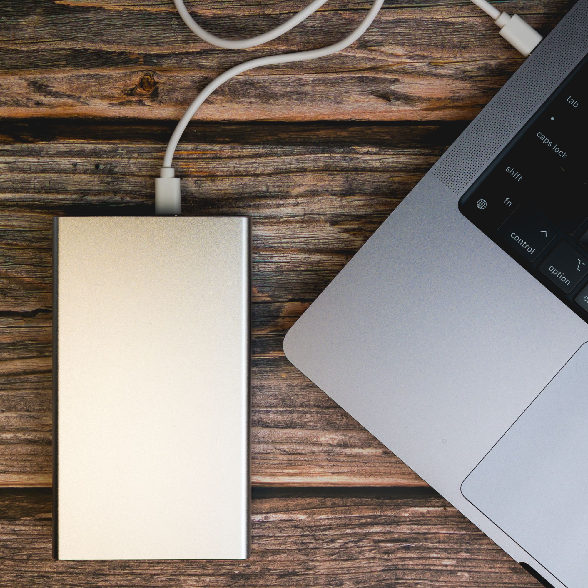 A power bank, labeled Ortega, with a sleek silver design, connected to a laptop via a charging cable.