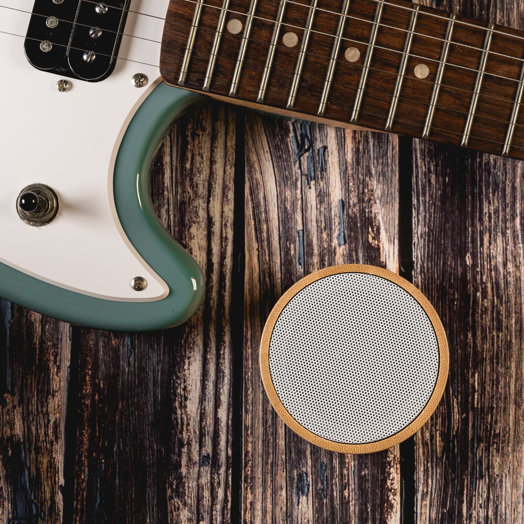 A Bluetooth speaker featuring a bamboo exterior, positioned beside an electric guitar on a wooden surface.