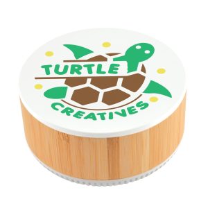 A round speaker made of bamboo with a white top featuring a turtle logo and the text "TURTLE CREATIVES."