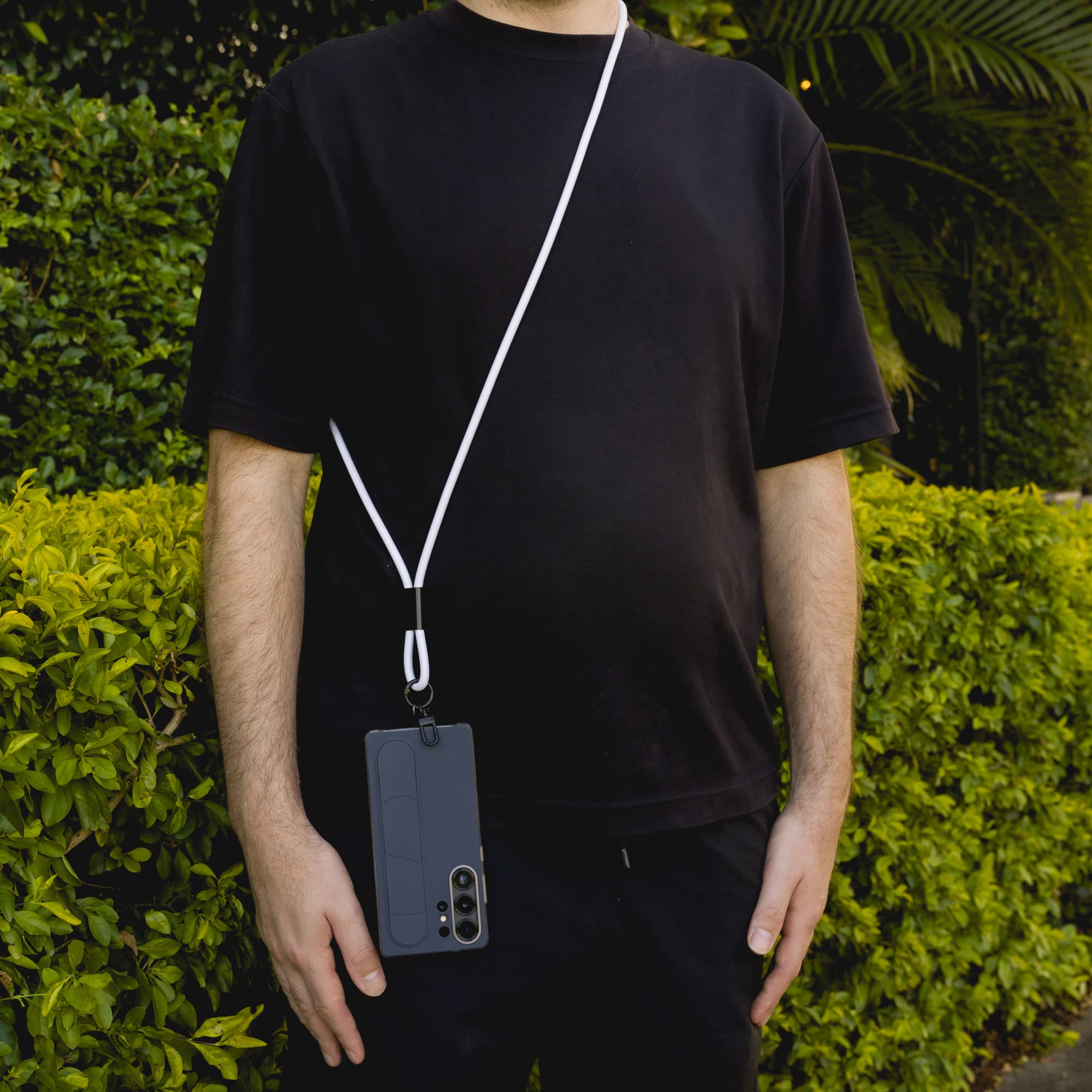 A phone lanyard in white, secured to a smartphone, is draped across a person’s body against a green background.
