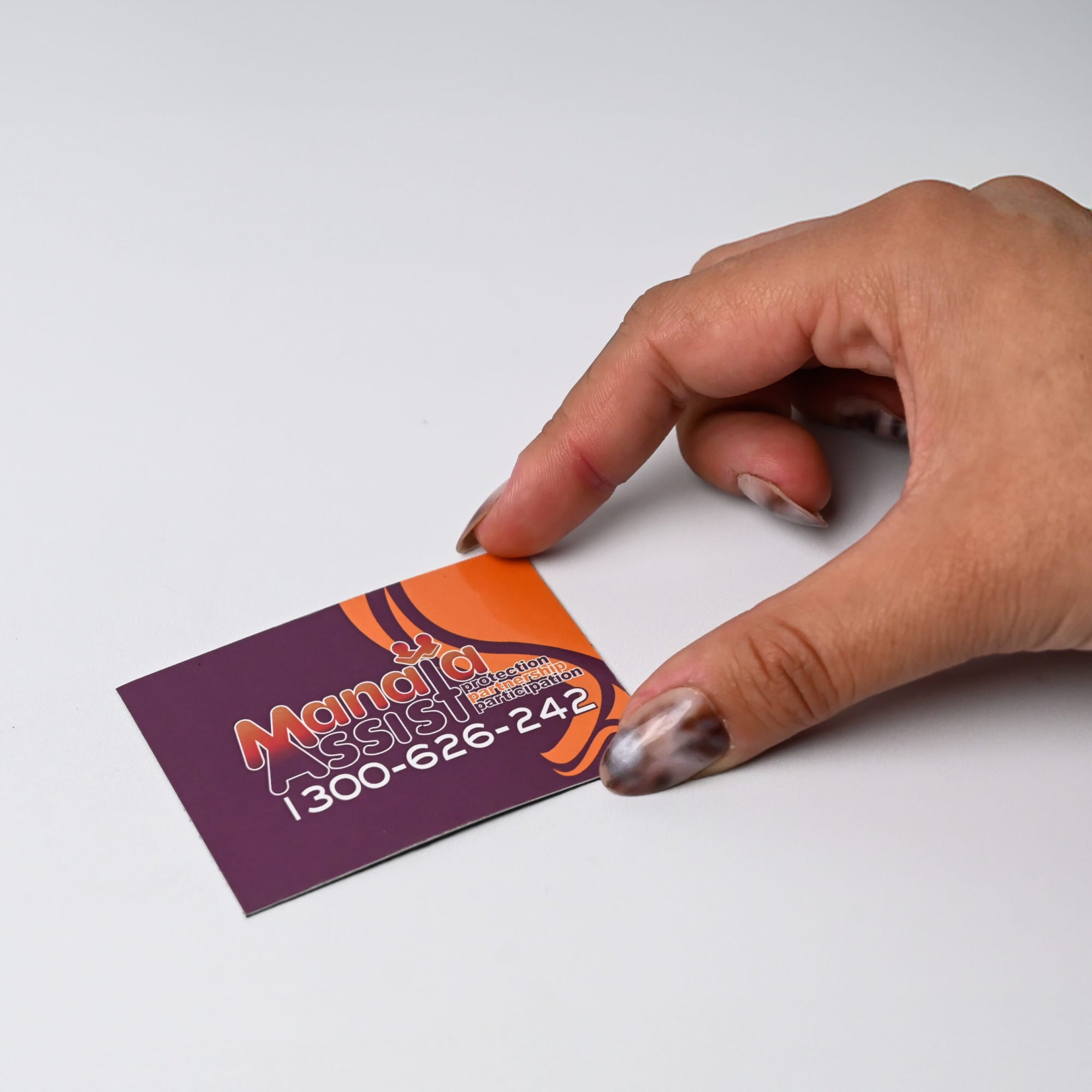 A hand holding a colourful business card featuring a logo and contact information on a plain white background.