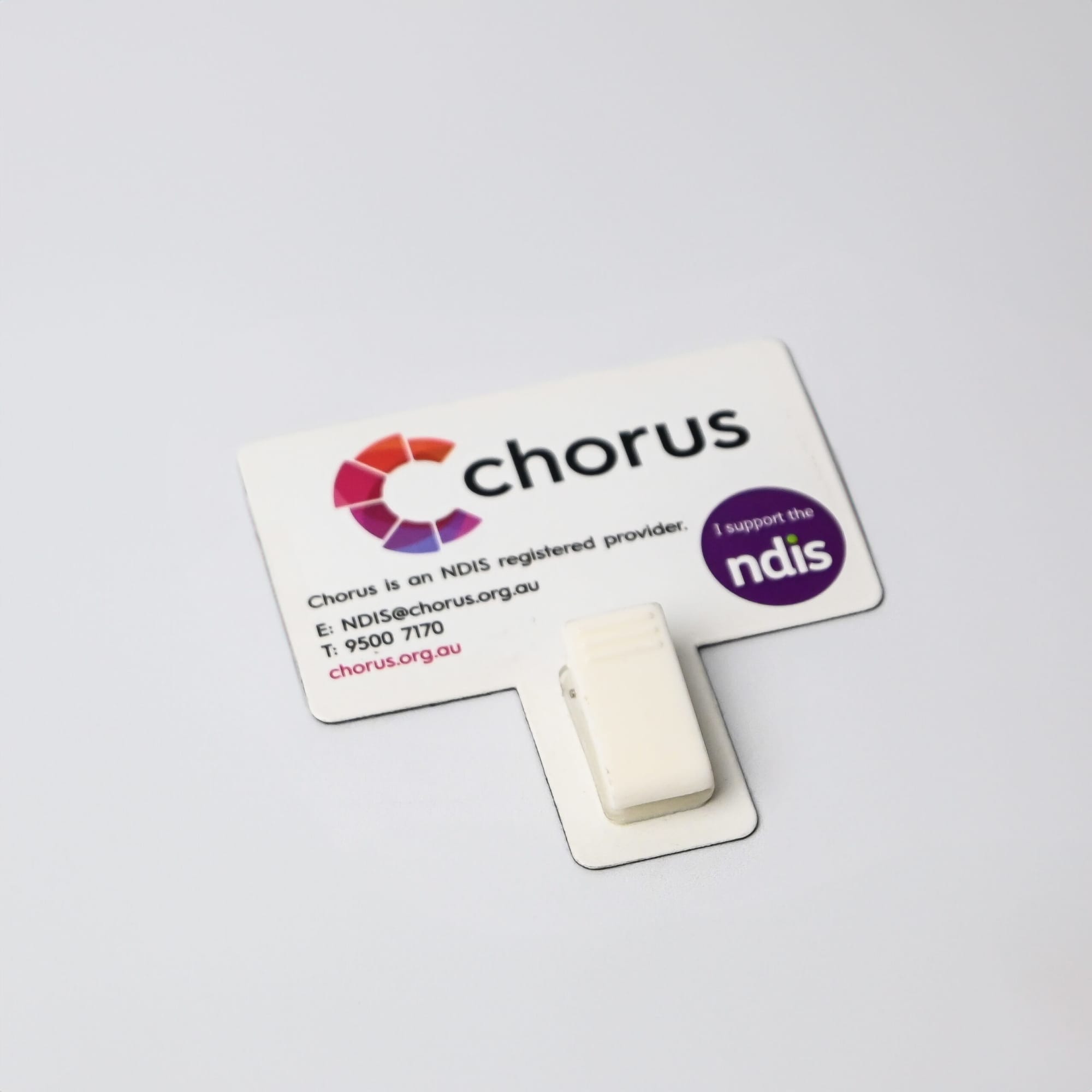 A white T-Magnet with a clip, attached to a printed card featuring logos and contact details.