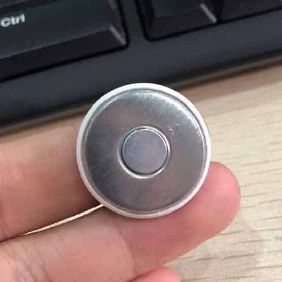 A hand holding a silver fridge magnet button badge against a wooden surface and a keyboard in the background.