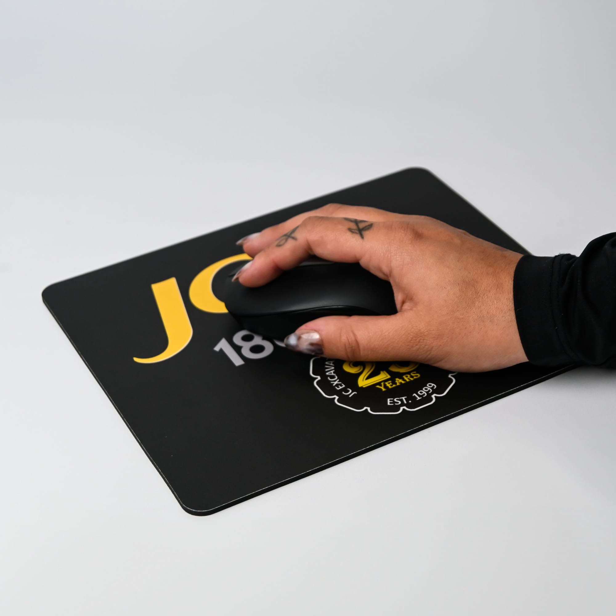 A black fabric mouse mat with a hand using a black mouse, featuring a logo and yellow text.