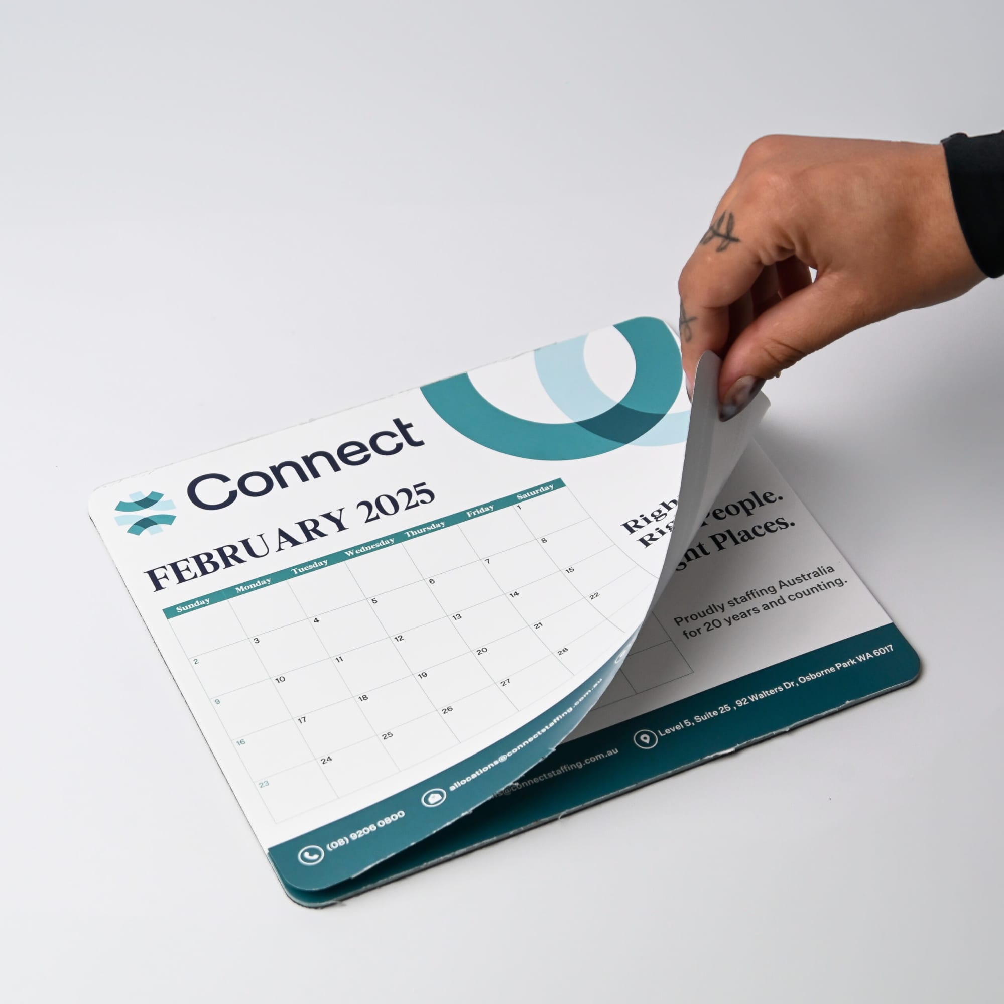 A mouse mat in light blue and white, featuring a calendar for February 2025 and a logo.