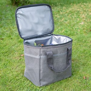 A grey nylon cooler bag with a silver interior, featuring handles and a mesh pocket, set on grass.
