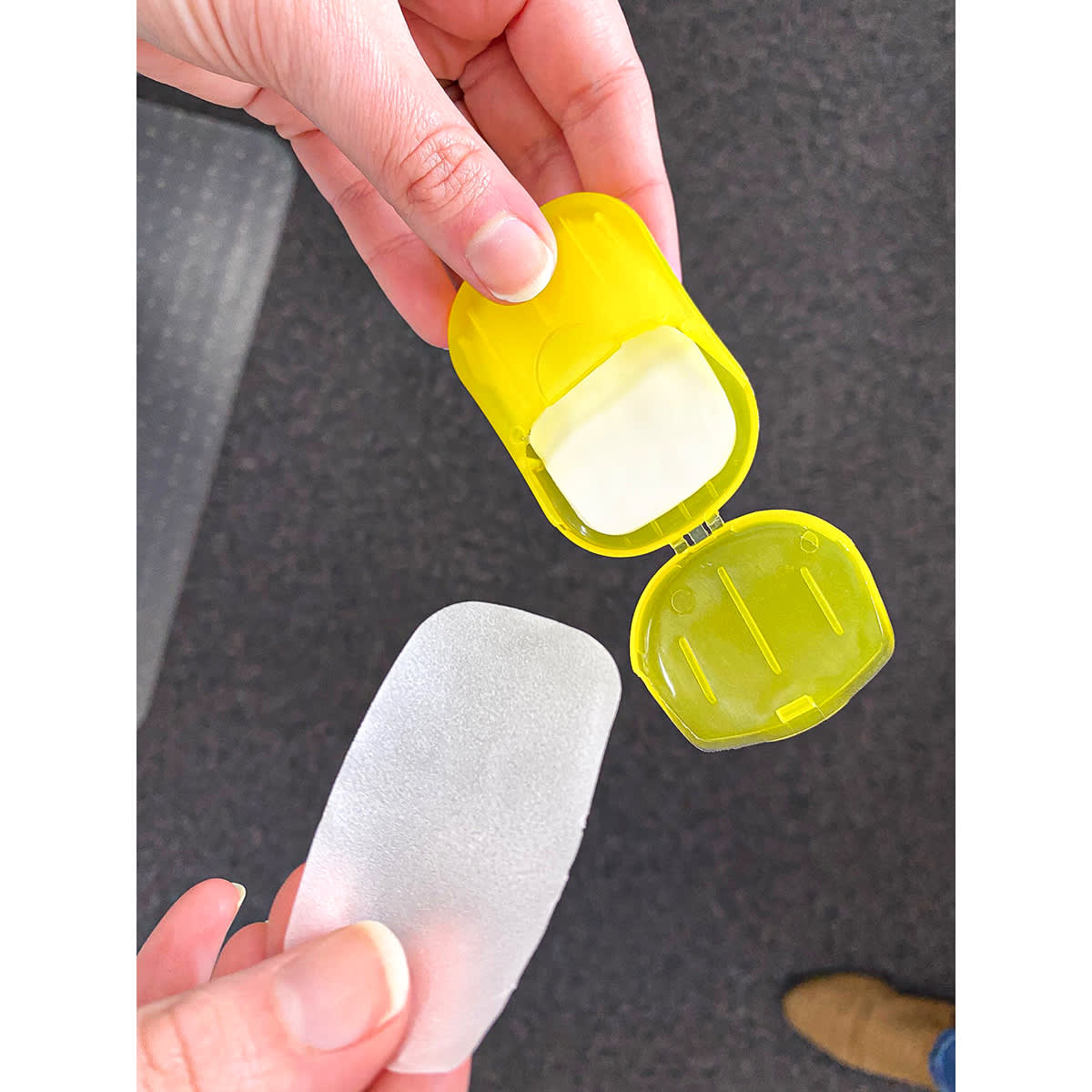 A yellow product container held in a hand, revealing a transparent, flexible pad inside.