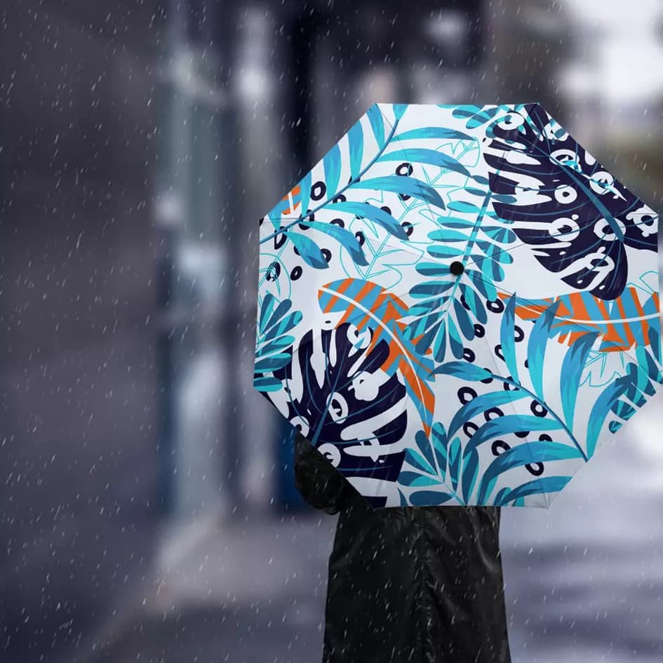 A full colour umbrella featuring a vibrant tropical leaf pattern in shades of blue, white, orange, and green.