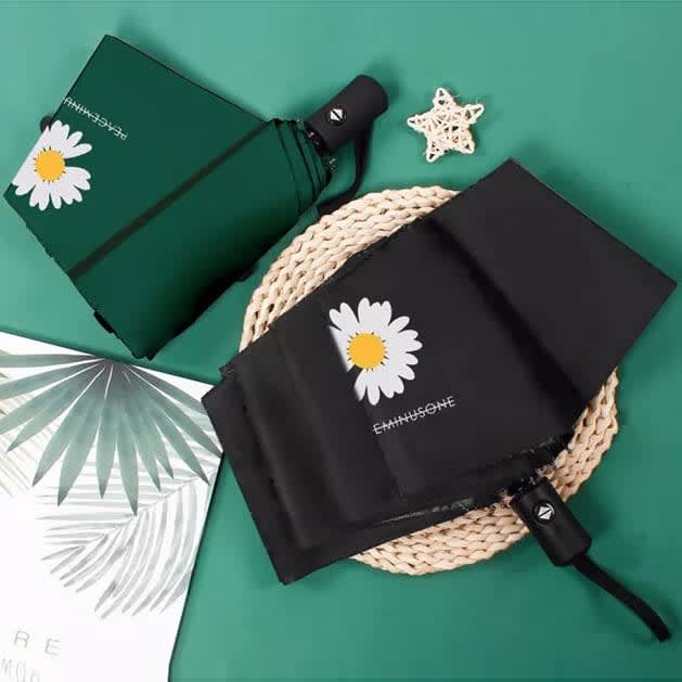 A black and green umbrella featuring a daisy design, resting on a woven mat with a starfish and decorative leaves.