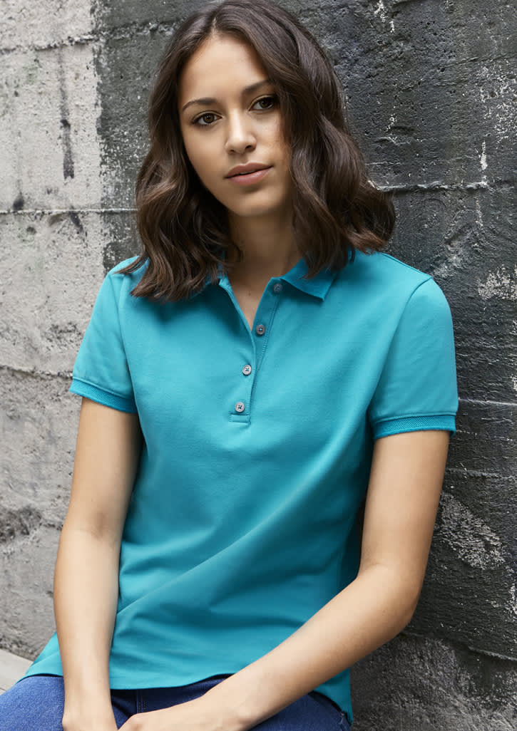 A turquoise women's short sleeve polo shirt featuring a collar and button detail, set against a textured grey background.