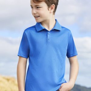 A blue short sleeve polo shirt on a young boy, standing outdoors with a scenic background. The shirt has a logo.