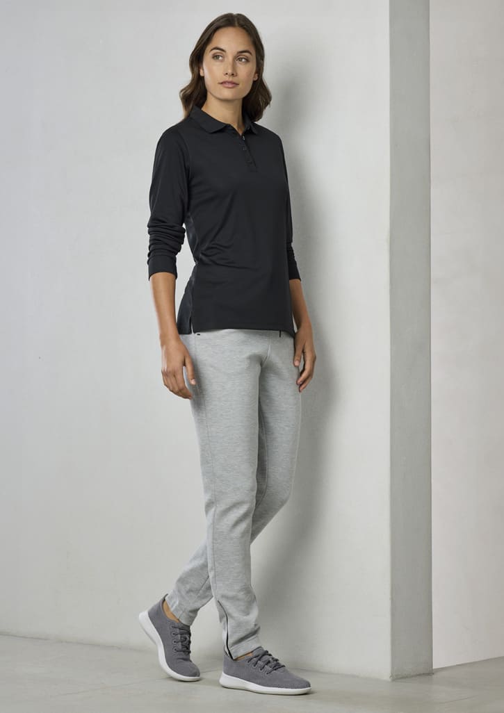 A woman stands wearing a black long sleeve polo shirt and grey joggers, with a logo on the shirt.