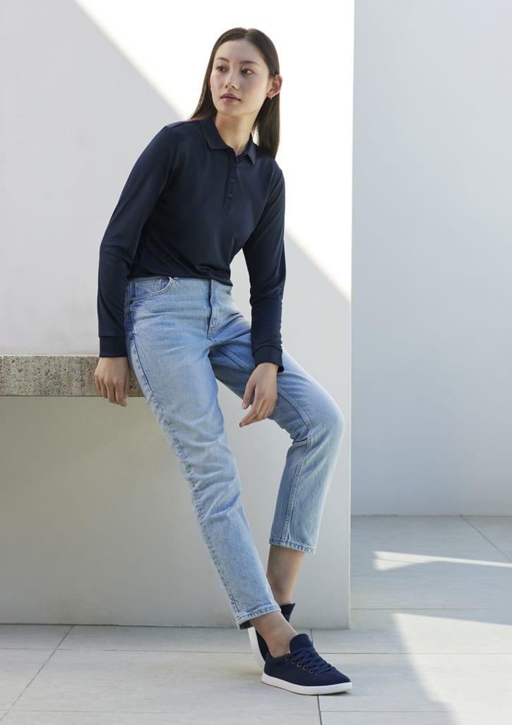 A long sleeve navy polo shirt worn with light blue jeans, paired with casual sneakers. The model is seated against a minimalist background.