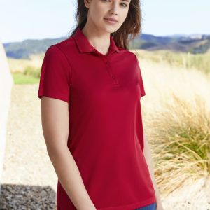 A red women's short sleeve polo shirt with a collar and buttons, set against a natural outdoor backdrop.