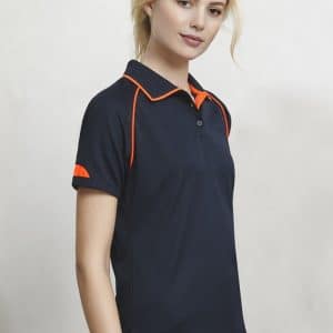 A navy blue women's polo shirt featuring orange accents on the collar and sleeves, with branding.