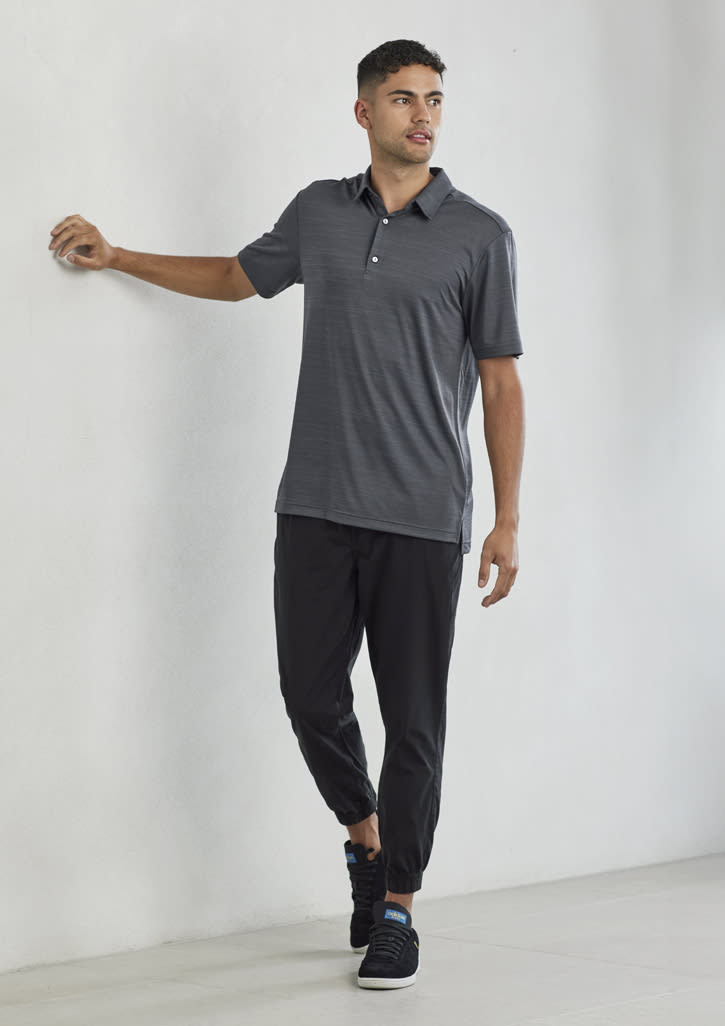 A men's short sleeve polo in grey, featuring a collar and a branding logo, paired with black pants and shoes.