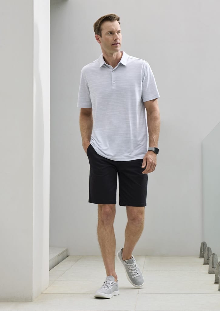 A light grey short sleeve polo shirt paired with black shorts and grey sneakers. The model is standing in a modern setting.