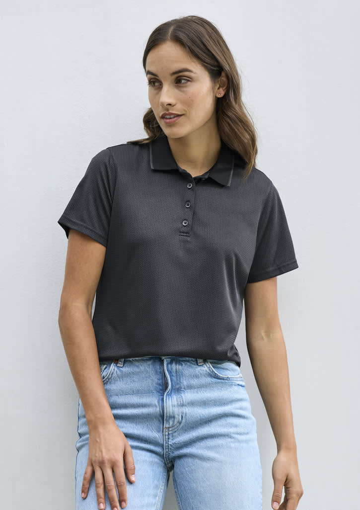 A woman is wearing a black short sleeve polo shirt, paired with light blue jeans, standing against a white background.