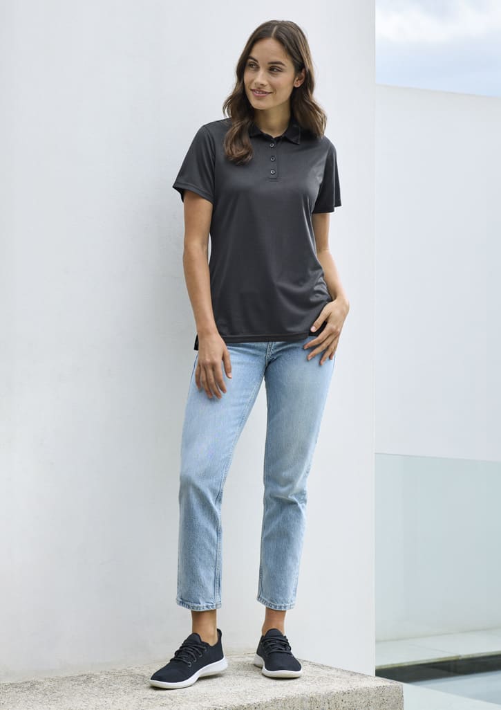 A dark grey women's polo shirt with short sleeves, paired with light blue jeans and black sneakers. The shirt features a logo.