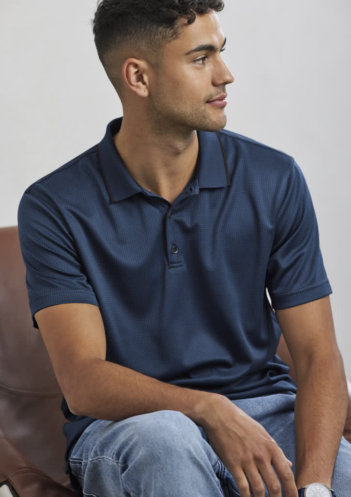 A navy blue short sleeve polo shirt with a logo, displayed on a seated male model.