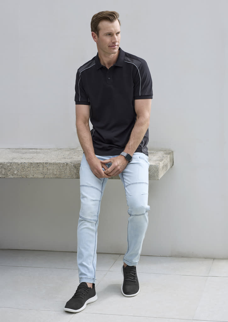 A man wearing a black short sleeve polo shirt with contrasting white accents, paired with light jeans and black sneakers.