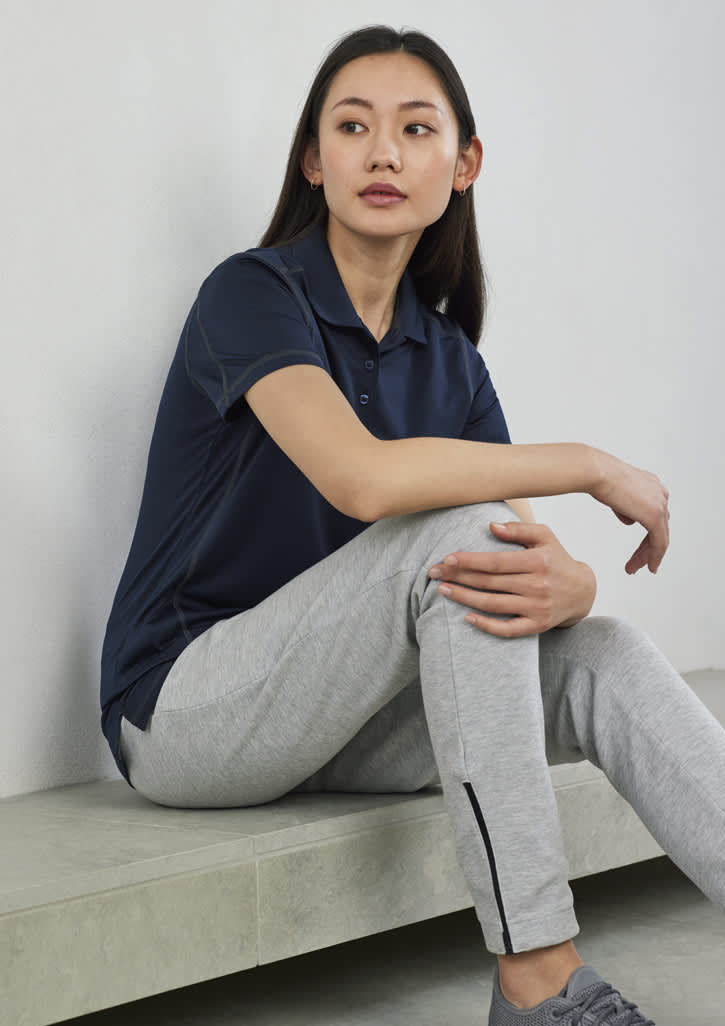 A navy women's short sleeve polo shirt, worn with grey sweatpants, displayed in a casual setting. It features a logo.