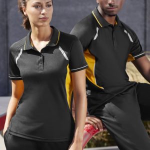 A black and yellow Women's Renegade Short Sleeve Polo, featuring a logo, displayed on a model against an urban backdrop.