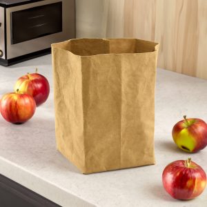 A kraft paper storage bag in a natural brown colour, surrounded by red apples on a kitchen countertop.
