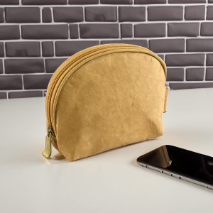 A yellow kraft paper cosmetic bag with a rounded shape and a zip closure, placed next to a smartphone.