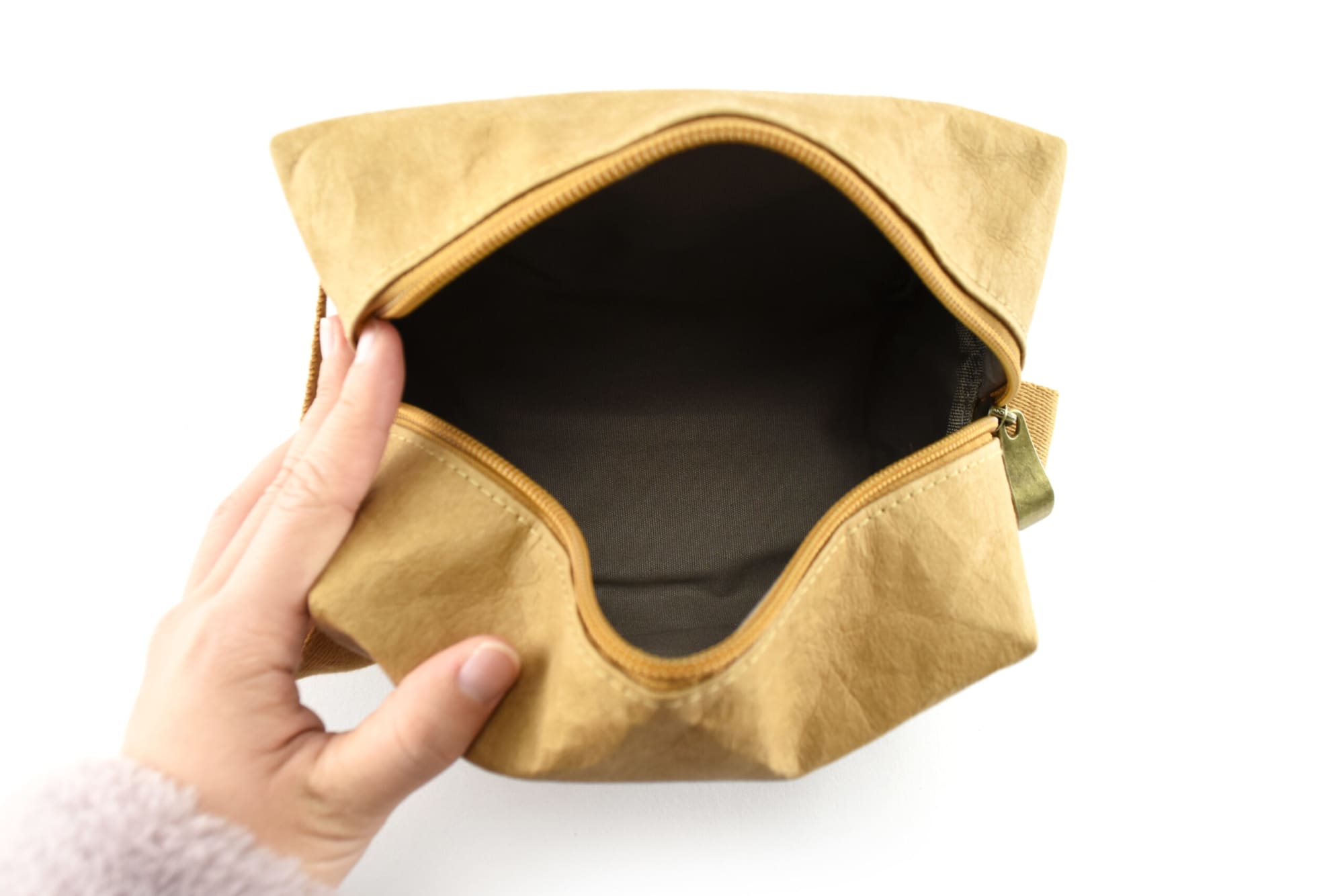 A kraft paper cosmetic bag in a light brown hue, featuring an unzipped opening with a fabric interior.