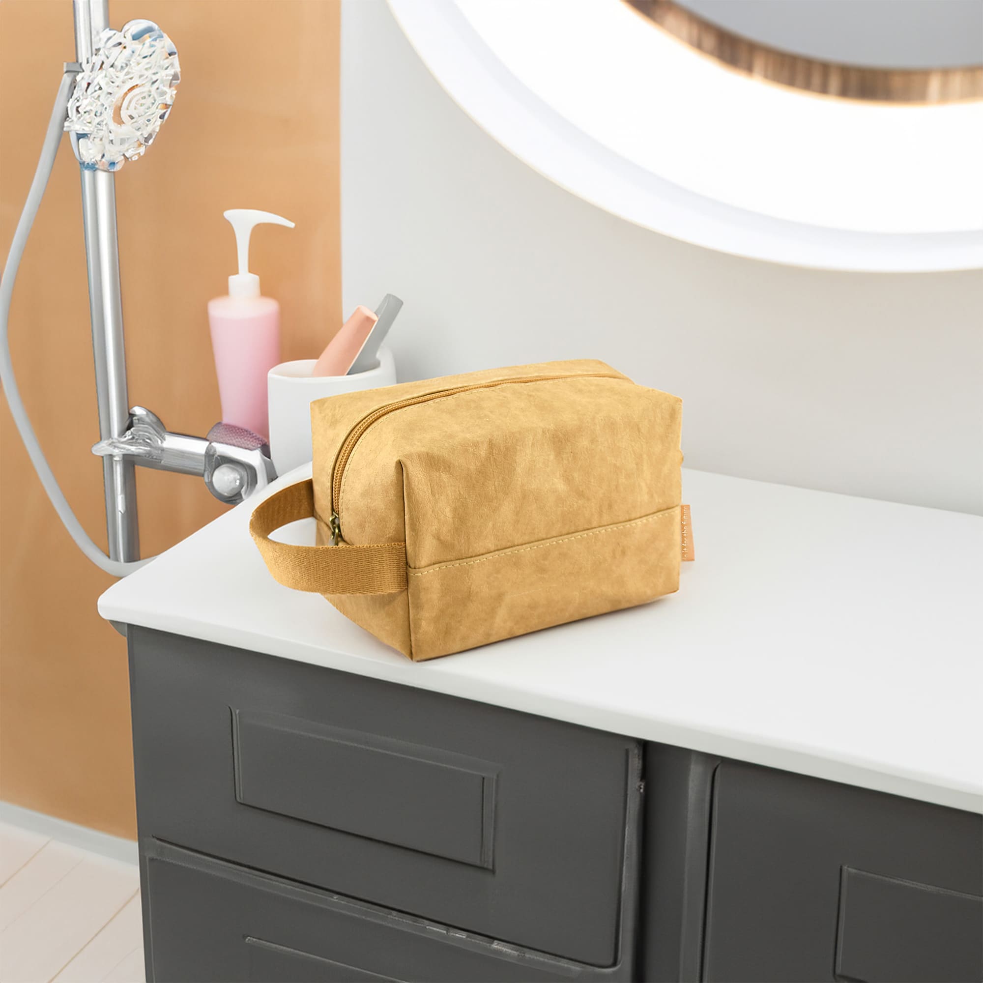 A kraft paper cosmetic bag in a warm yellow tone, placed on a bathroom countertop next to various toiletries.