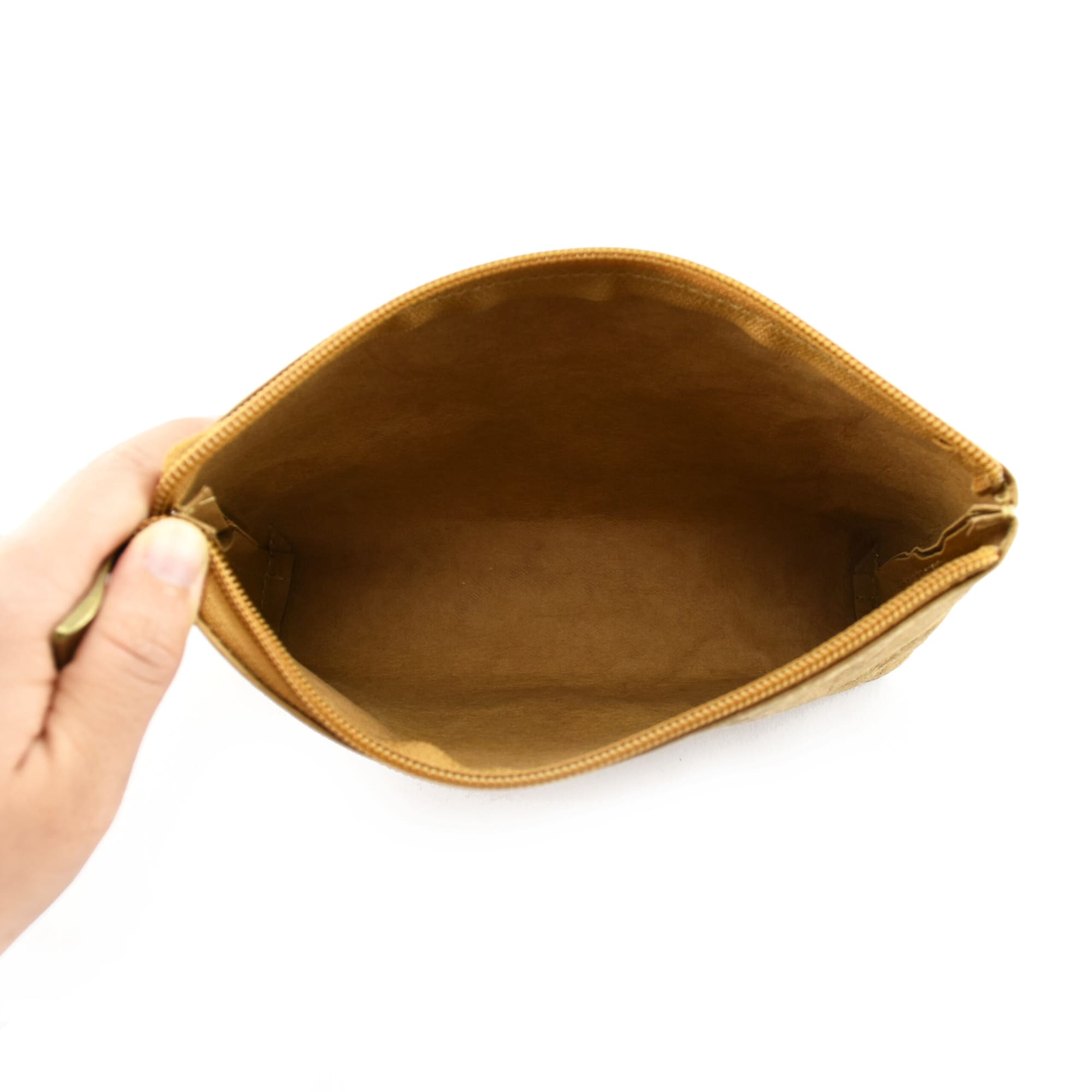 A hand holds a tan Kraft paper cosmetic bag, showcasing its spacious, empty interior. The bag features a zip closure and branding.