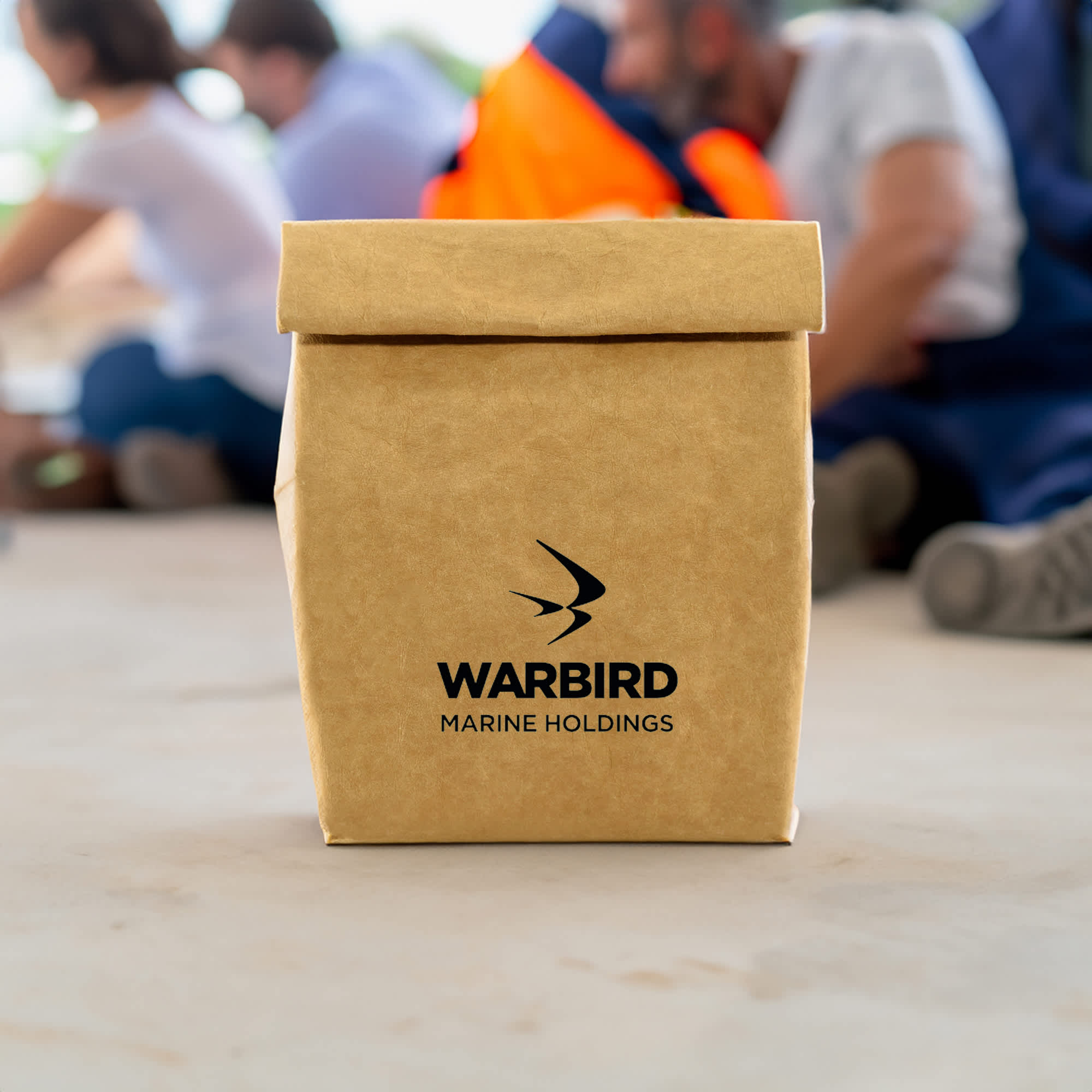 A kraft paper cooler bag in brown with a logo, placed on a surface in a casual setting.