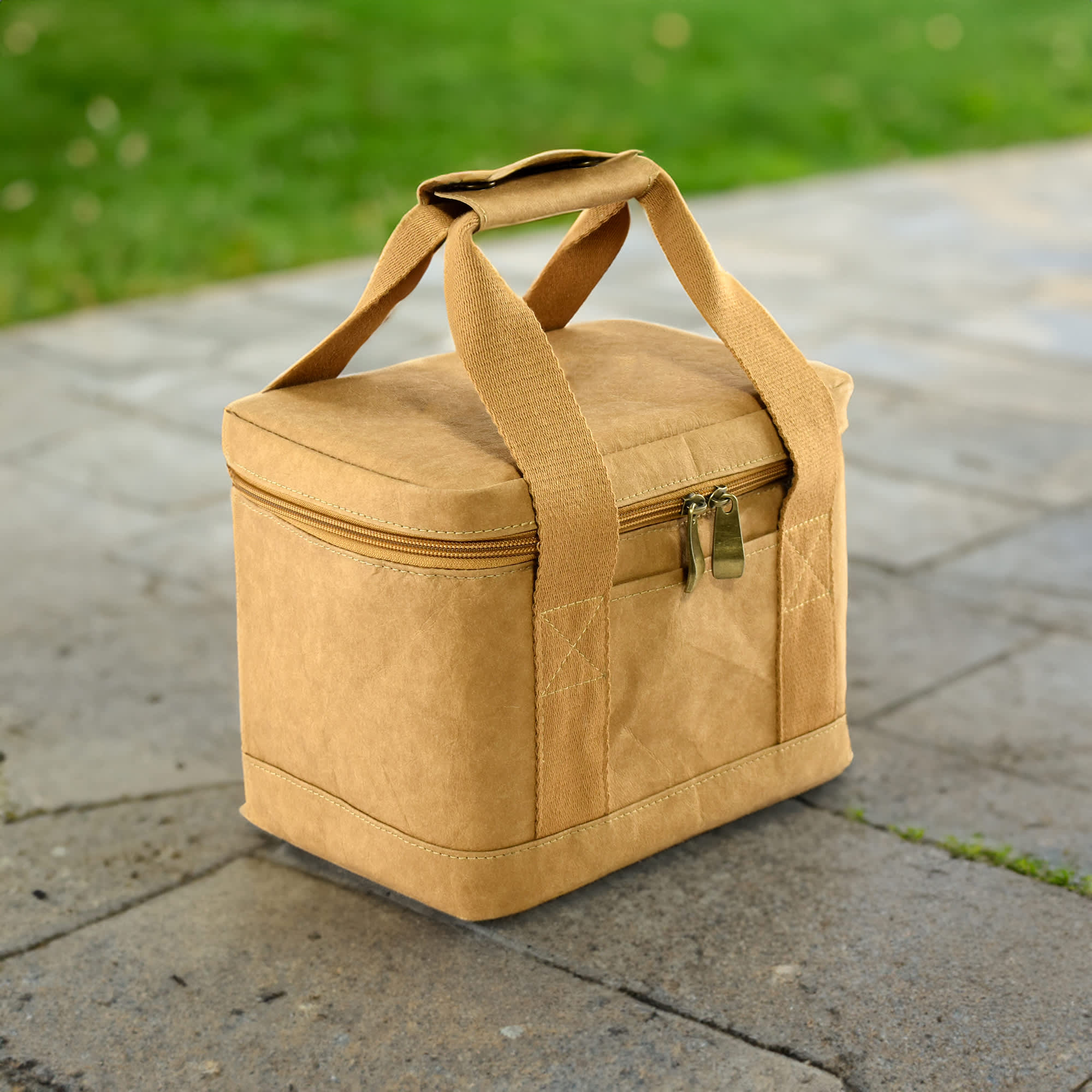 A tan kraft paper lunch cooler bag with a zippered closure and sturdy handles, placed on a stone surface.