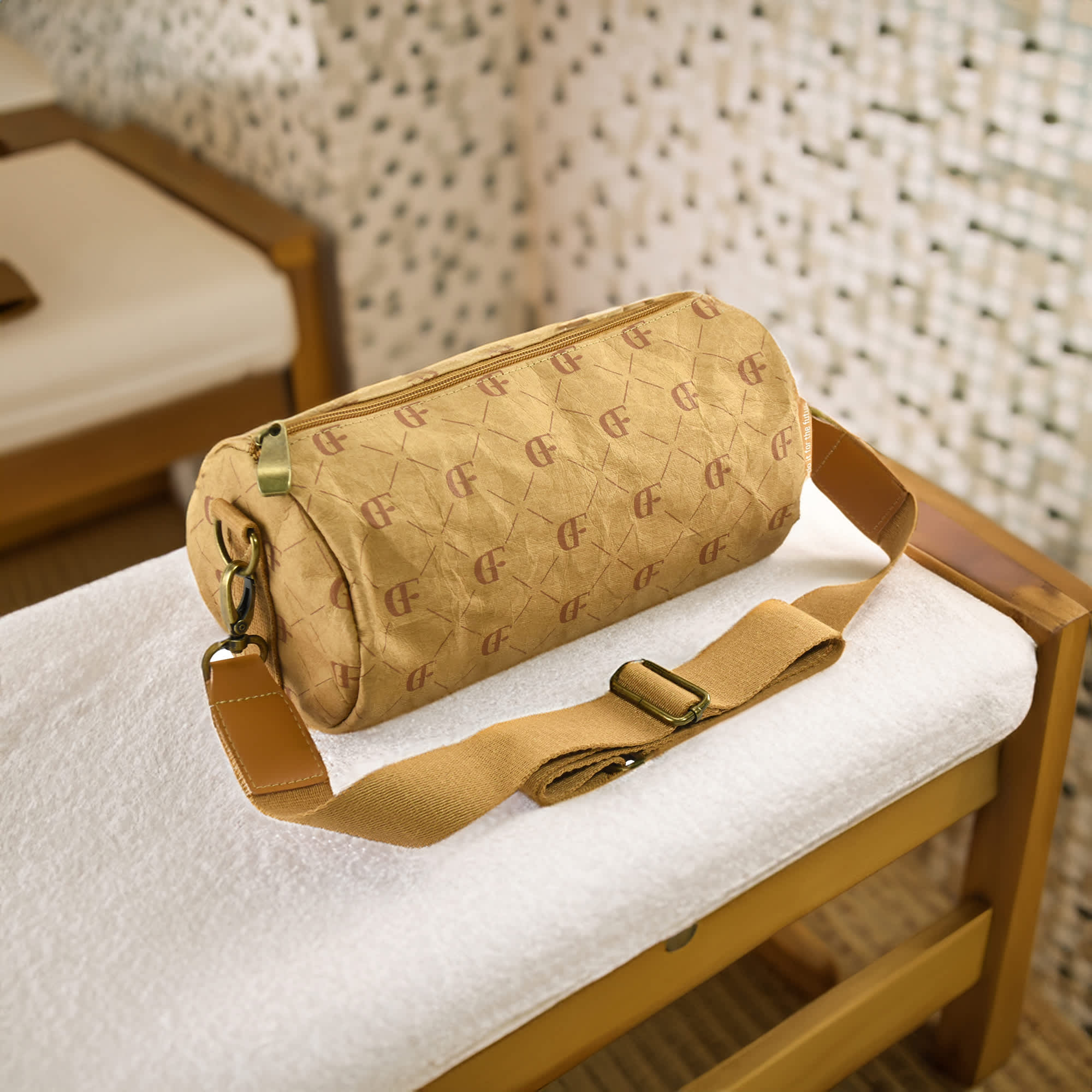 A cylindrical, ochre duffle bag with a logo, featuring a shoulder strap, placed on a white towel.
