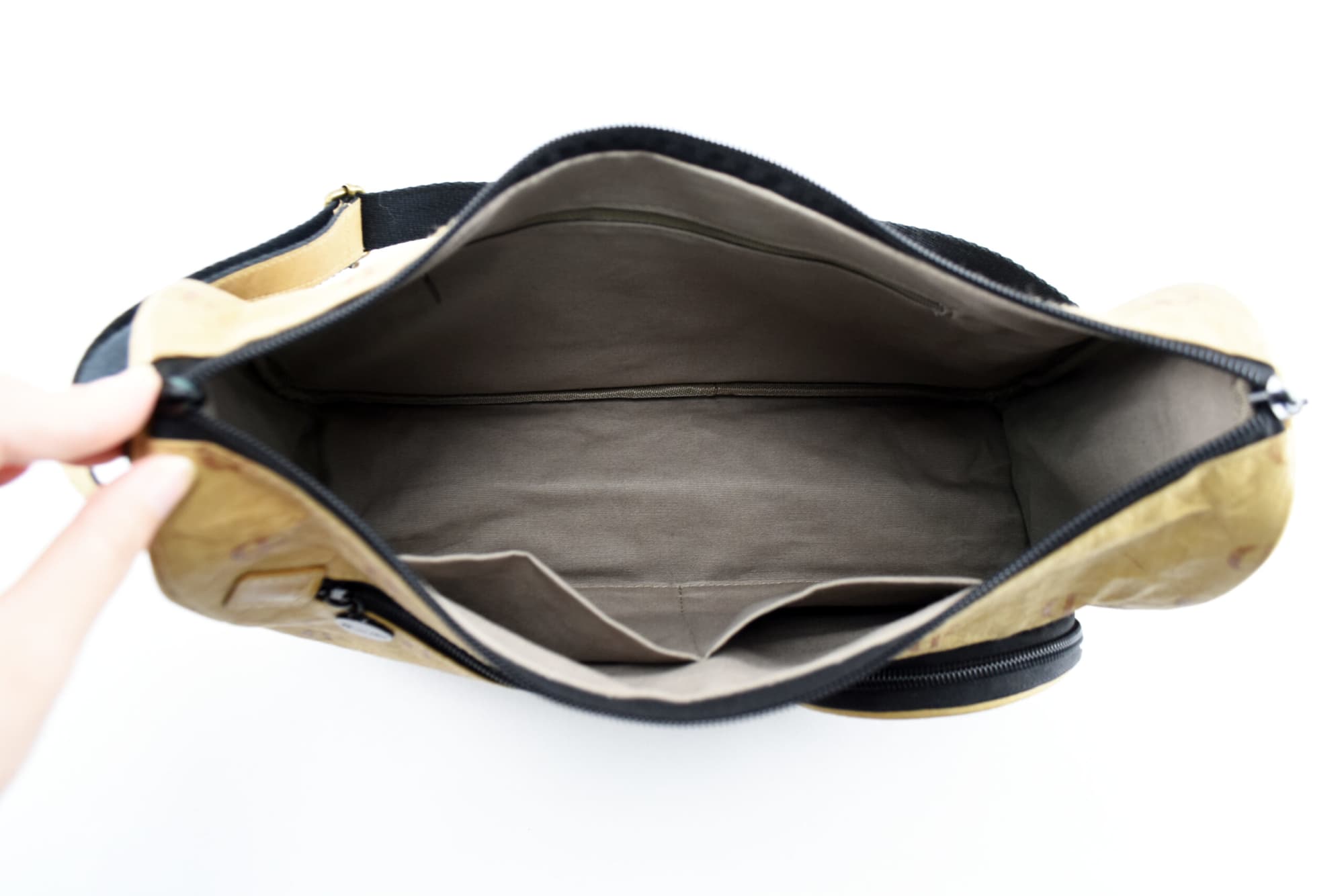 A kraft paper sling bag in tan with a black strap, featuring multiple compartments inside.