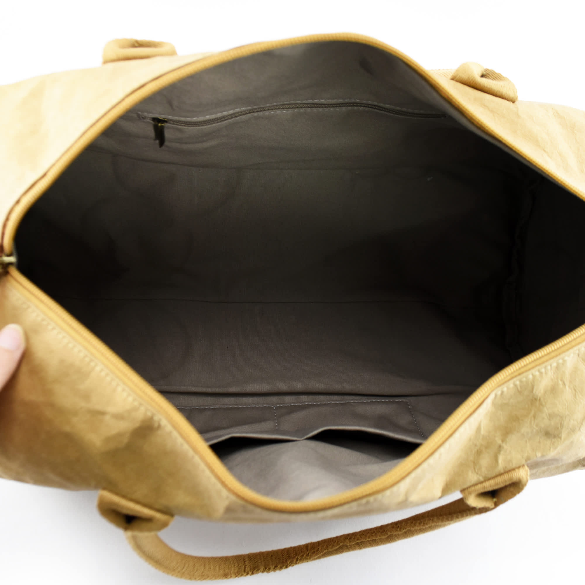 A tan kraft paper duffle bag with a spacious interior and zip closure, featuring inner pockets and a logo.