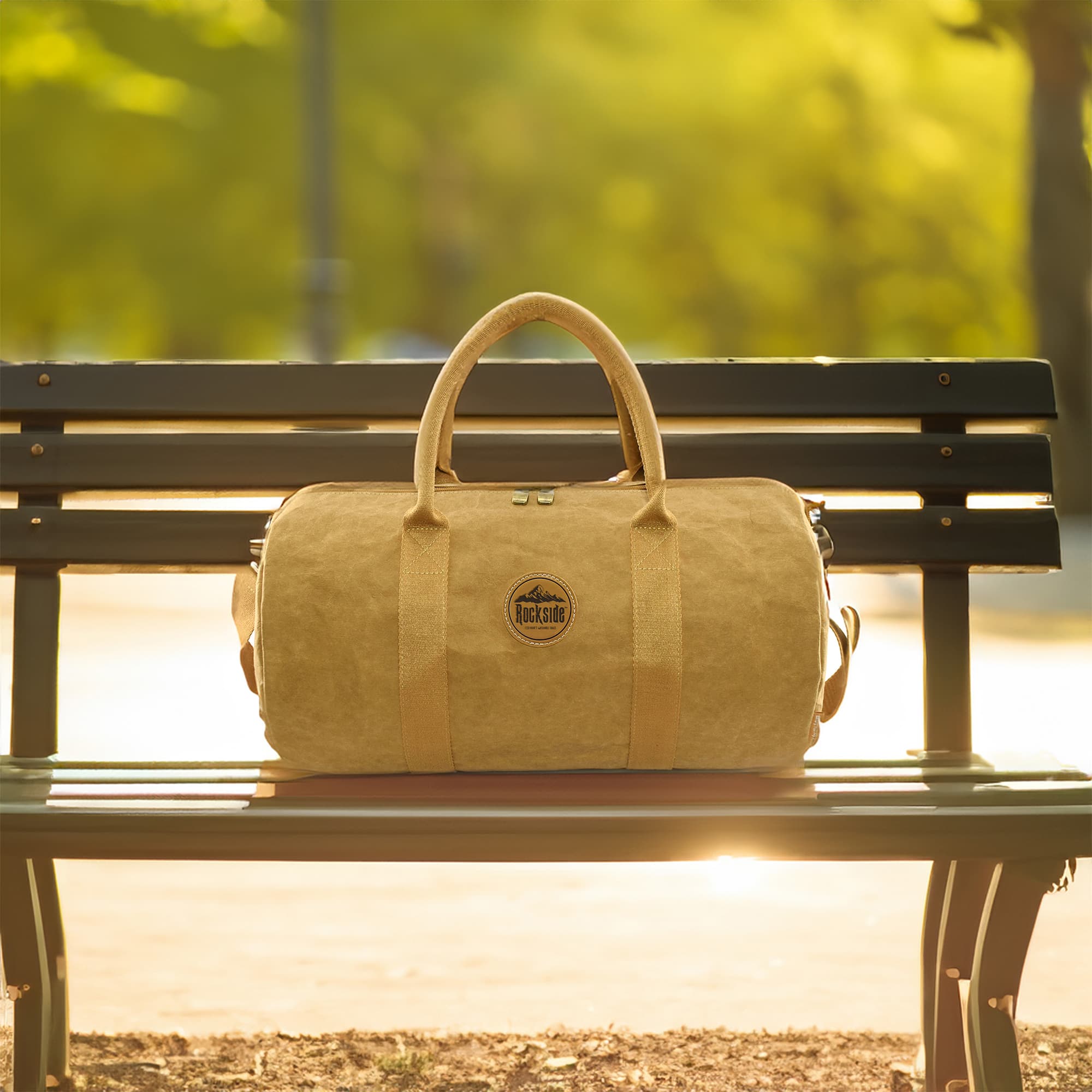 A kraft paper duffle bag in natural brown, featuring sturdy handles and a logo, resting on a park bench.