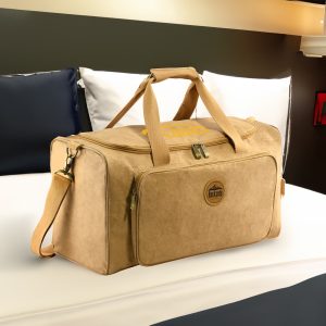 A kraft paper duffle bag in tan with handles and a detachable shoulder strap, placed on a bed.