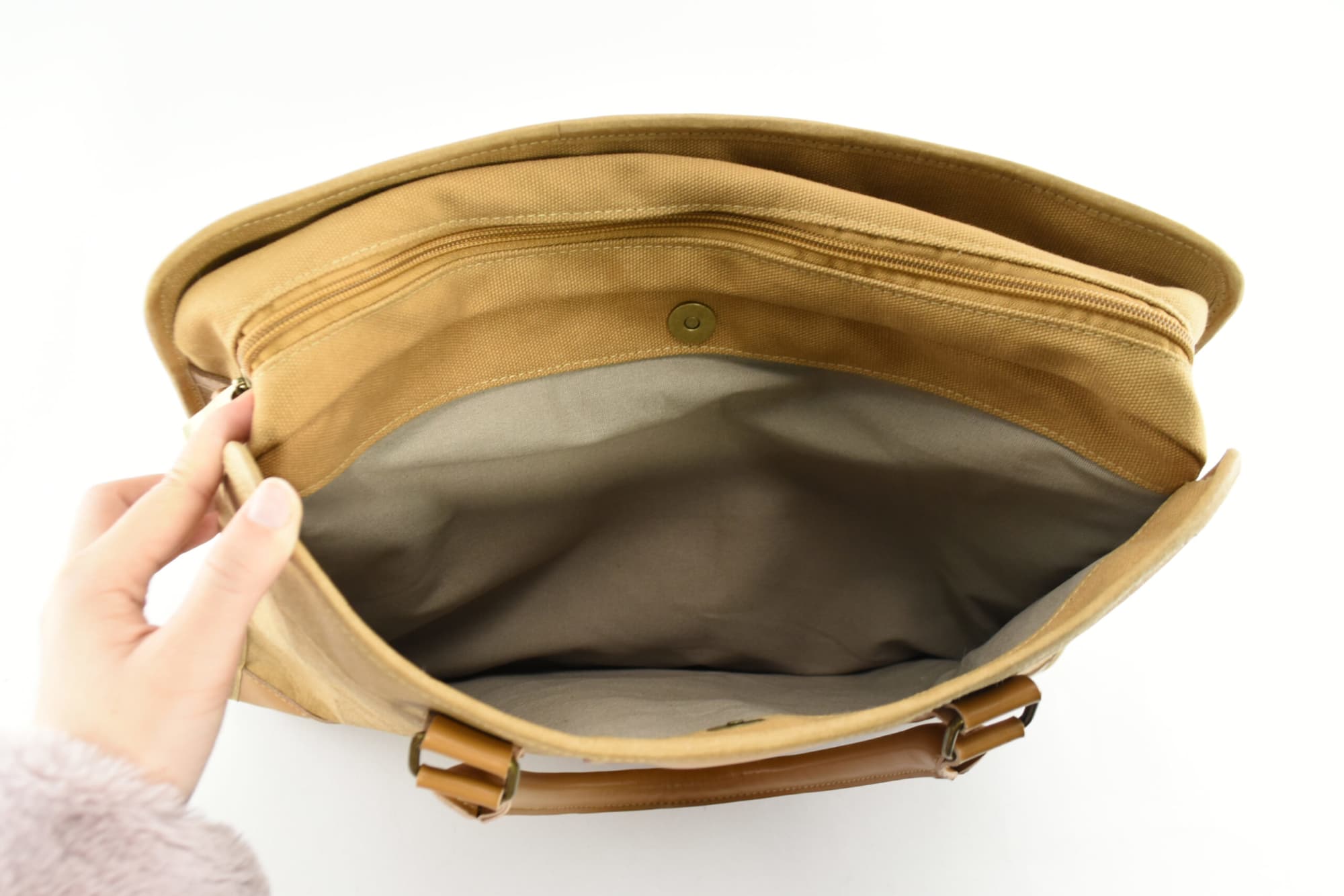 A tan kraft paper satchel with a spacious interior and a zippered pocket, featuring a closure button.