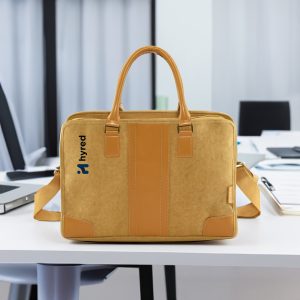 A yellow kraft paper satchel with tan accents and a logo, placed on a desk in an office setting.