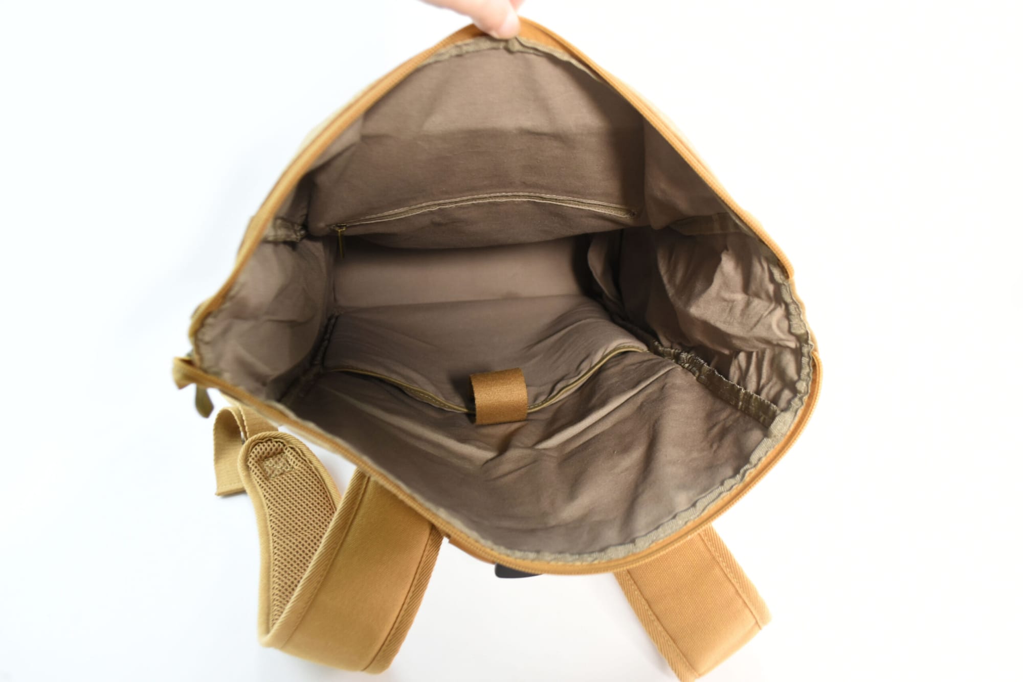 A tan kraft paper laptop backpack with an unzipped interior showing compartments and fabric lining.