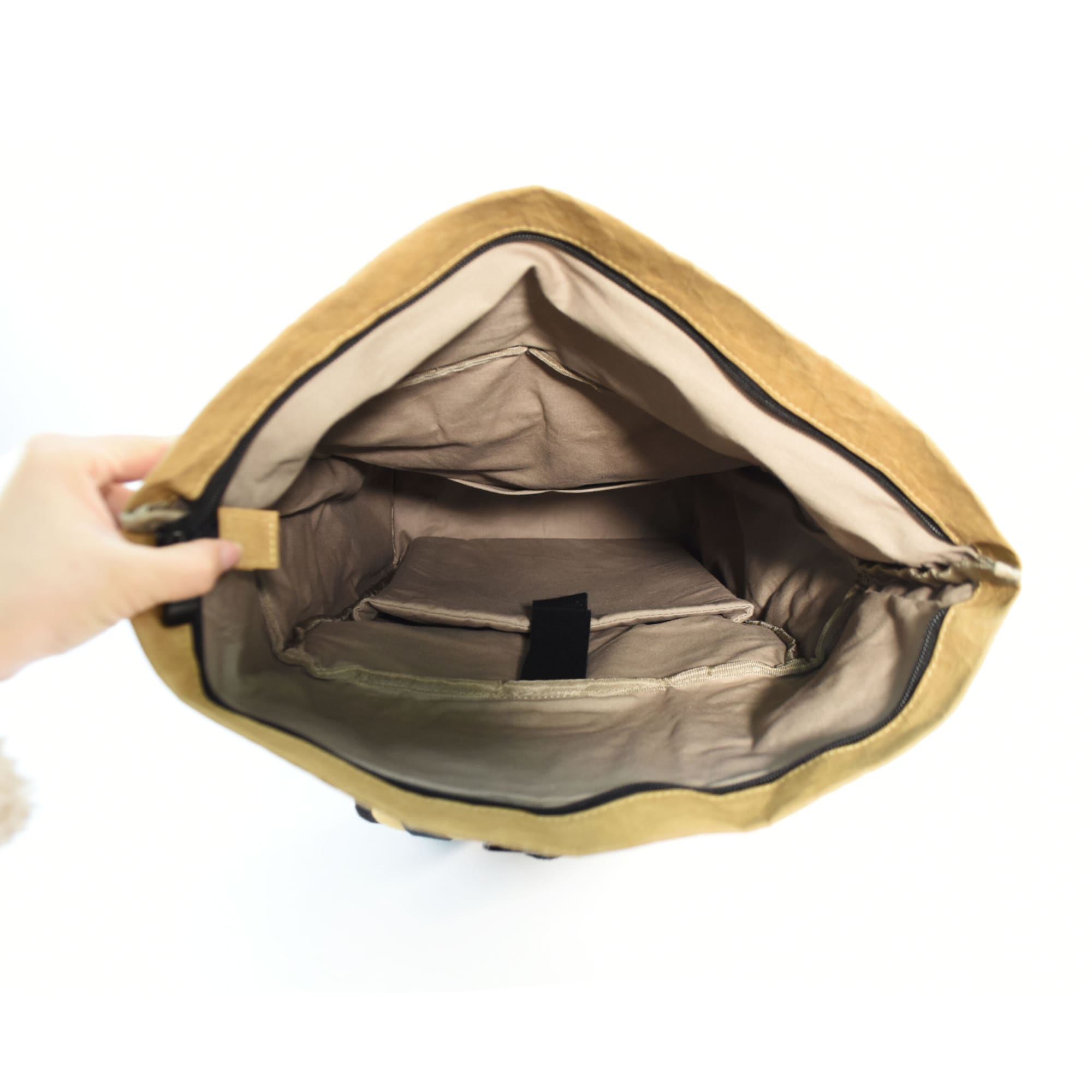 An open kraft paper laptop backpack in tan, showcasing the interior compartments and beige lining.