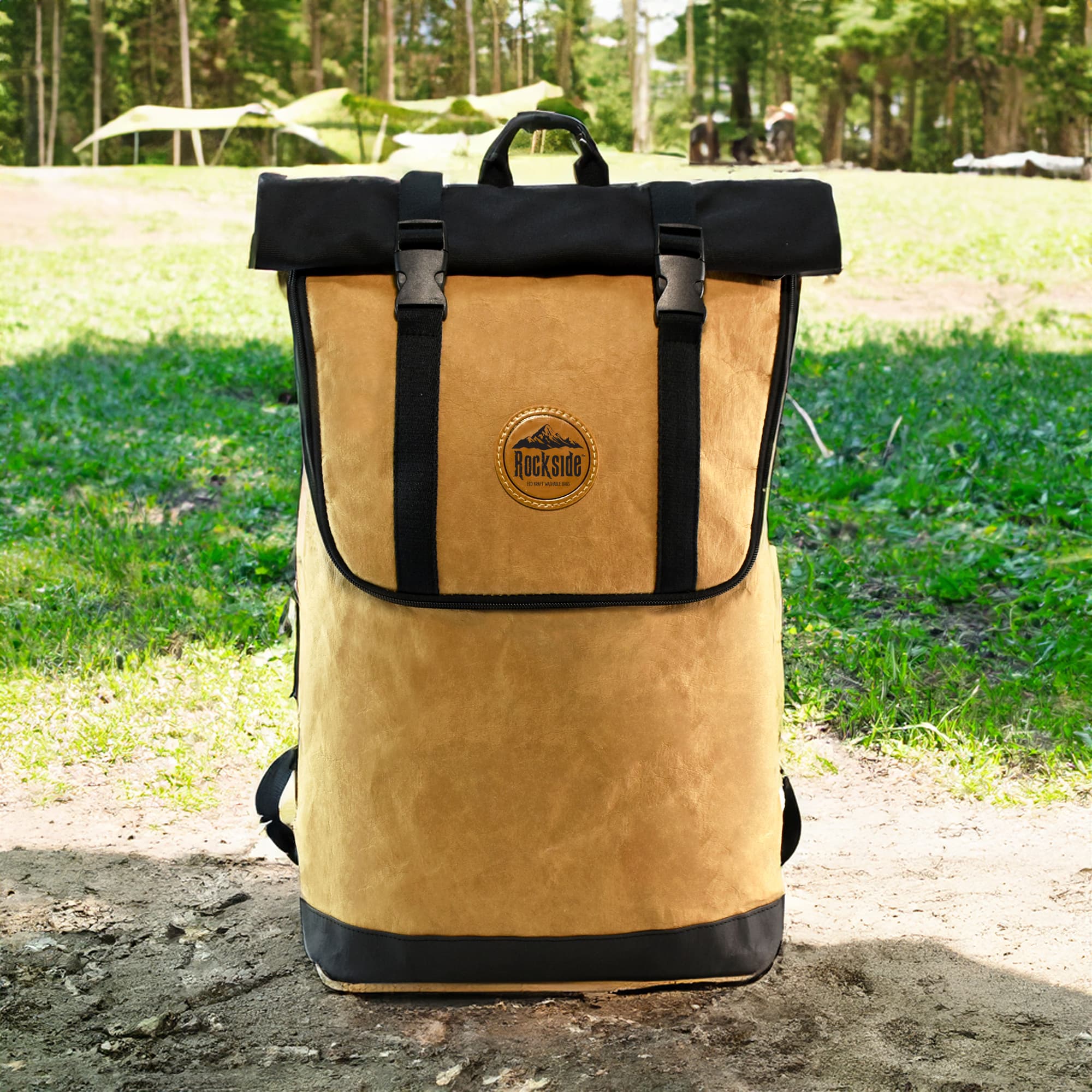 A tan and black backpack with a roll-top design and a logo, set against a natural outdoor background.