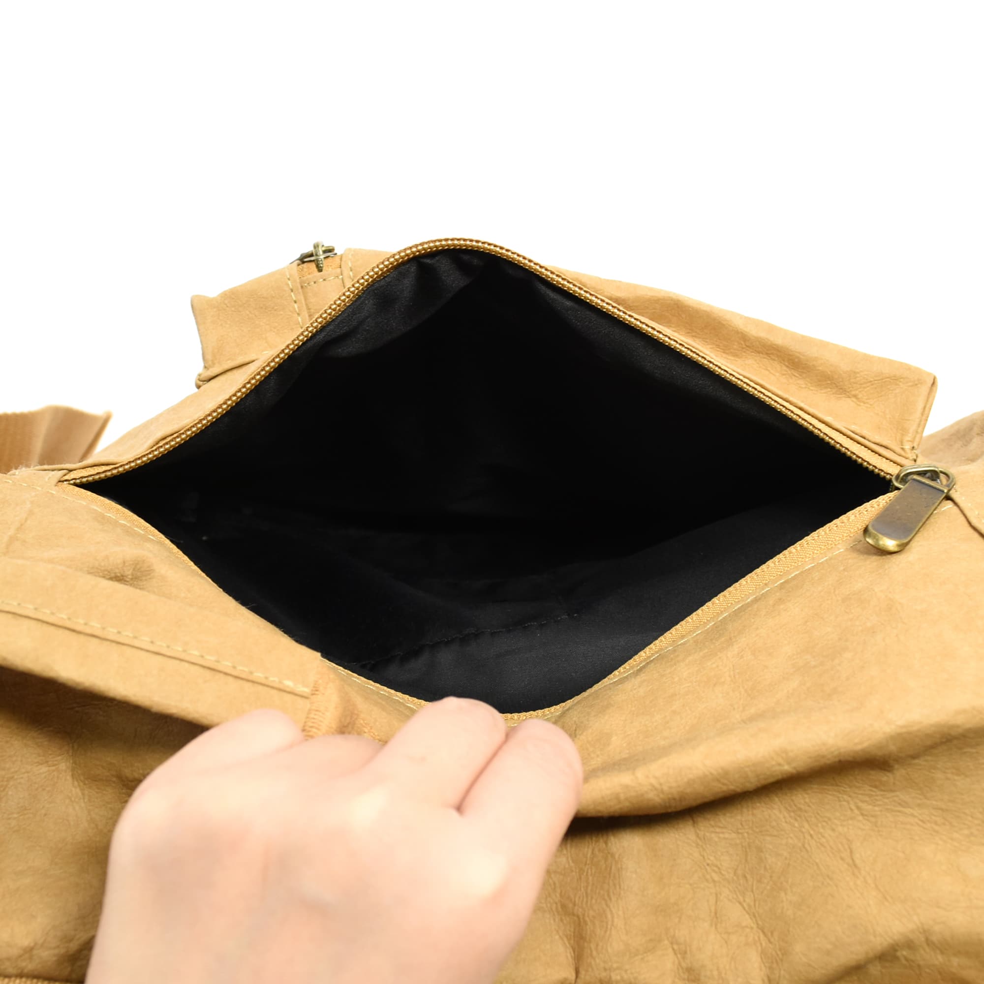 A hand reaching into a tan kraft paper laptop backpack, revealing a black interior and a zippered opening.