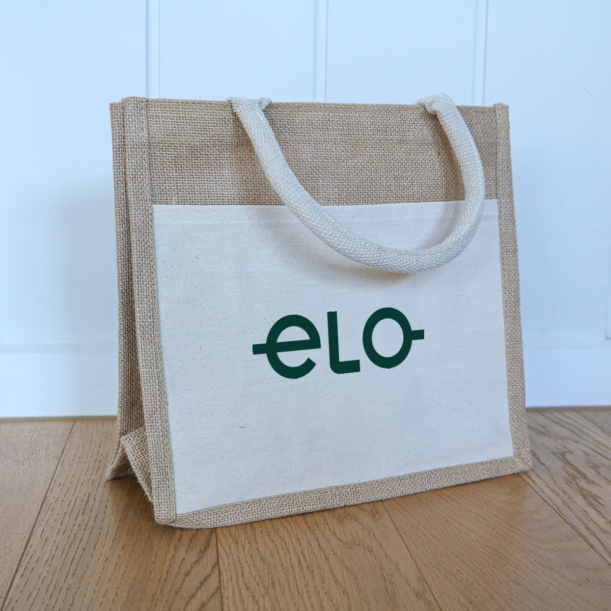 A jute tote bag in natural and cream colours, featuring a logo on the front and two handles.
