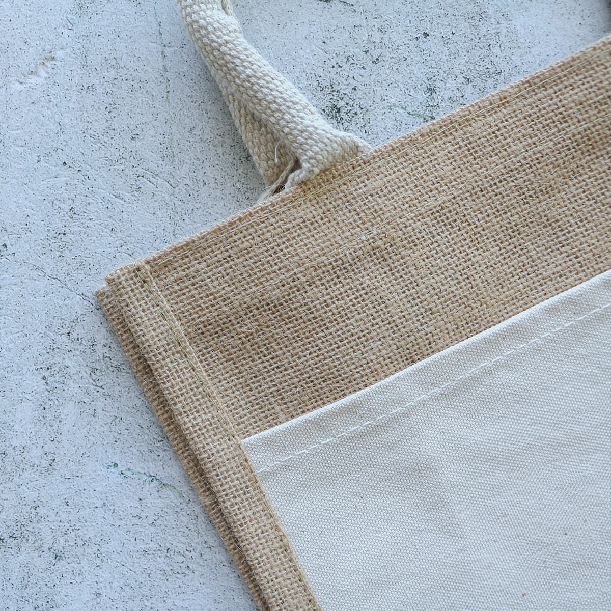 A jute tote bag featuring a natural burlap texture with a cream canvas section and sturdy handles.